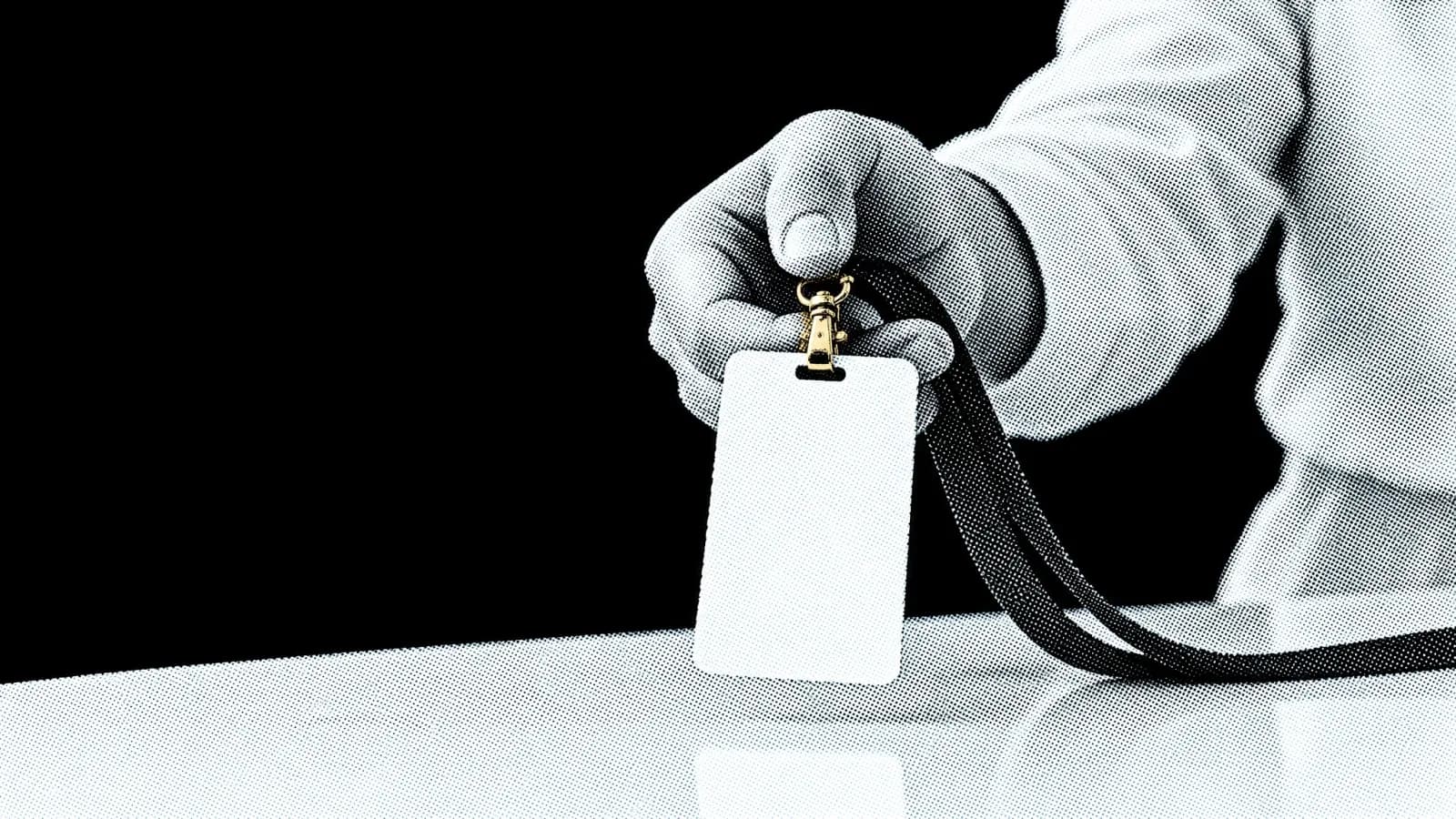A hand holding out a blank security badge on a lanyard across a counter